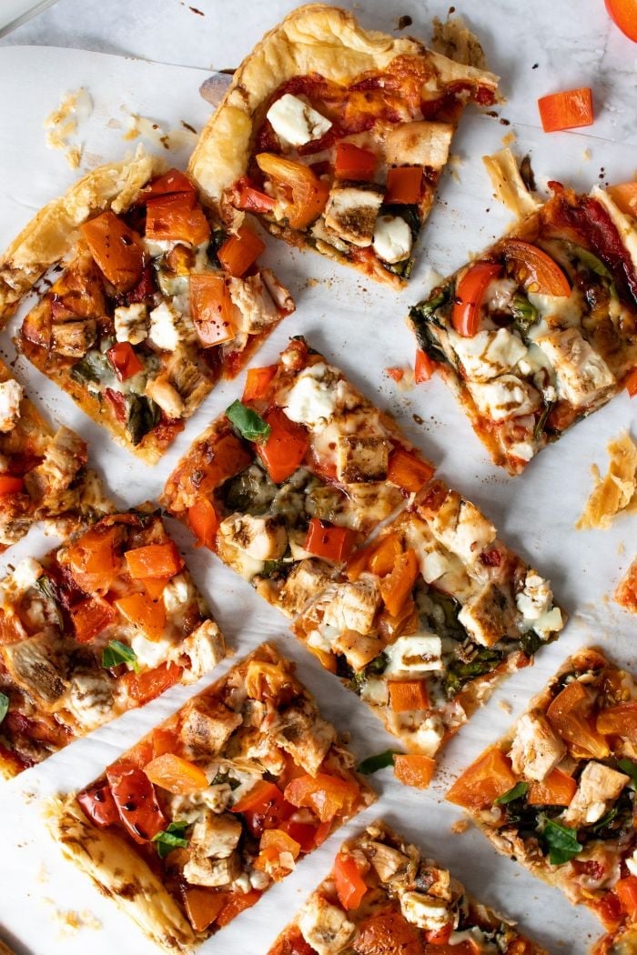 the puff pastry pizza is cut up into squares and spread apart on a piece of parchment paper